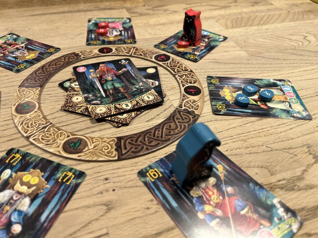 A cardboard ring, surrounded by seven cards with illustrations of venerable vikings. The player pieces, a wooden owl and crow, stand atop certain cards.